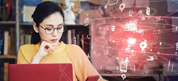 Junge Frau arbeitet am Laptop, in der rechten Bildhälfte schwebt ein Hologramm