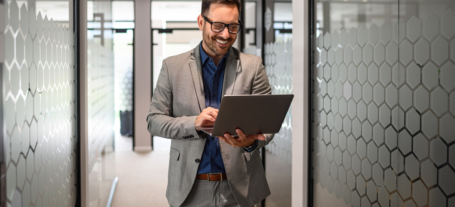 Portrait of developer smiling and doing online research over laptop while walking in office corridor